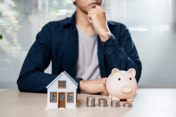 A thoughtful person considers financial planning with piggy bank and house model